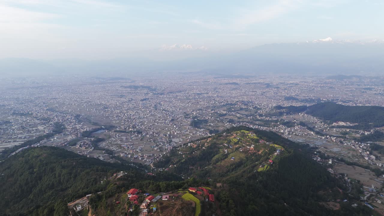 Drone view of Kathmandu Valley reveals its dense urban layout, surrounding green hills, and distant Himalayan horizon, capturing the unique blend of culture, terrain, and city life in Nepal