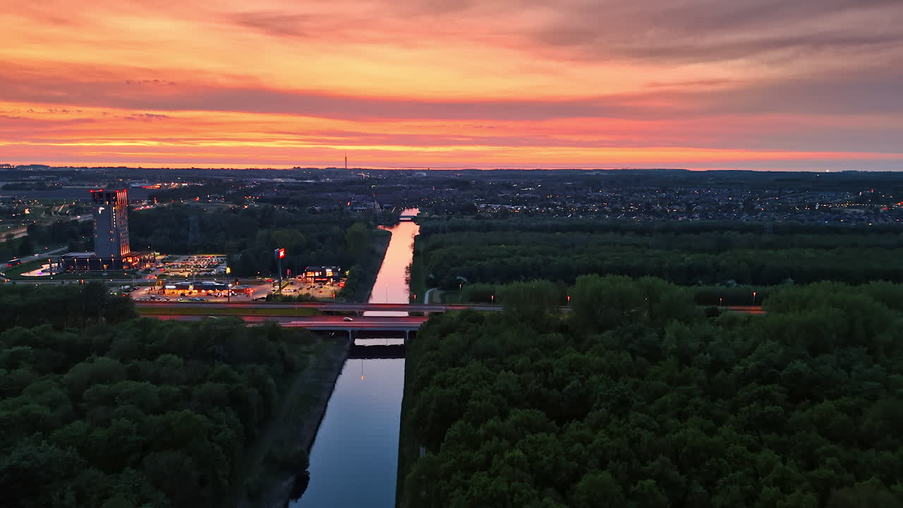 City lights by sunset river. Vibrant sunset casts colorful reflections on a calm river, while city lights begin to twinkle along the water's edge