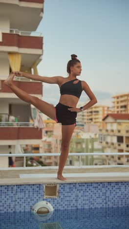 woman practicing yoga on a rooftop near a swimming pool