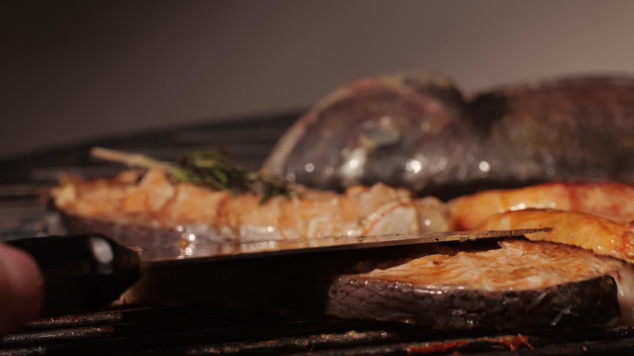 Chef cooking red salmon fish steaks with oil and spices on grill close-up. Prawns on fire throwing them on pan. Making Dorado fishes on frying grill. Restaurant Food concept. Sea food barbecue.