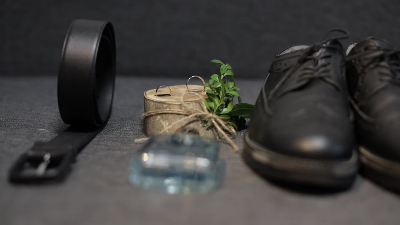 los detalles de la boda del novio. el perfume del novio, el cinturón, los zapatos y los anillos de bodas se encuentran en el sofá.