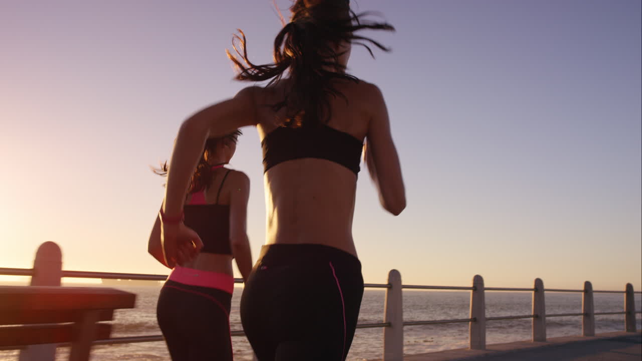 dos mujeres atléticas corriendo al aire libre en cámara lenta en el paseo marítimo al atardecer cerca del océano disfrutando de la carrera nocturna