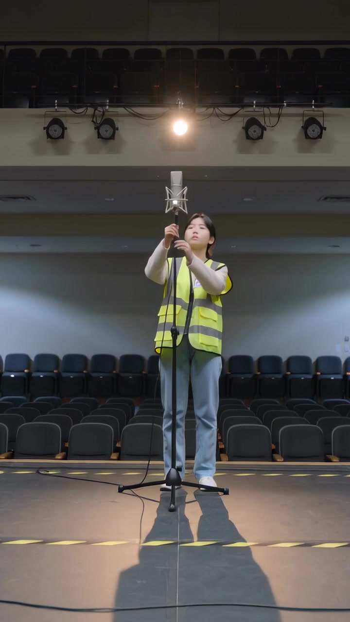 Vertikal video: Teenager i sikkerhedsvest løfter og justerer mikrofon i shock mount på scenen før show.