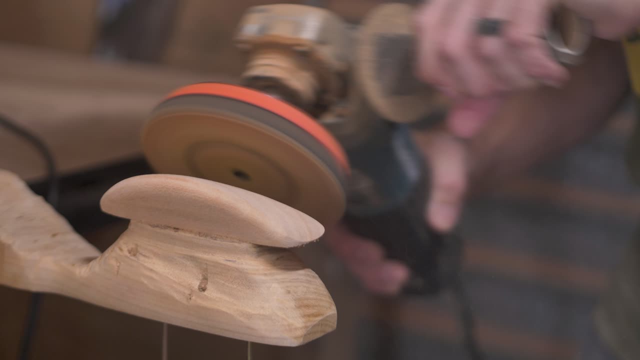 Slow motion close-up of man with ring and tattoos using electric orbital grinder power tool to sand and shape wooden indoor climbing holds at DIY garage woodwork shed in Australia carpentry industry