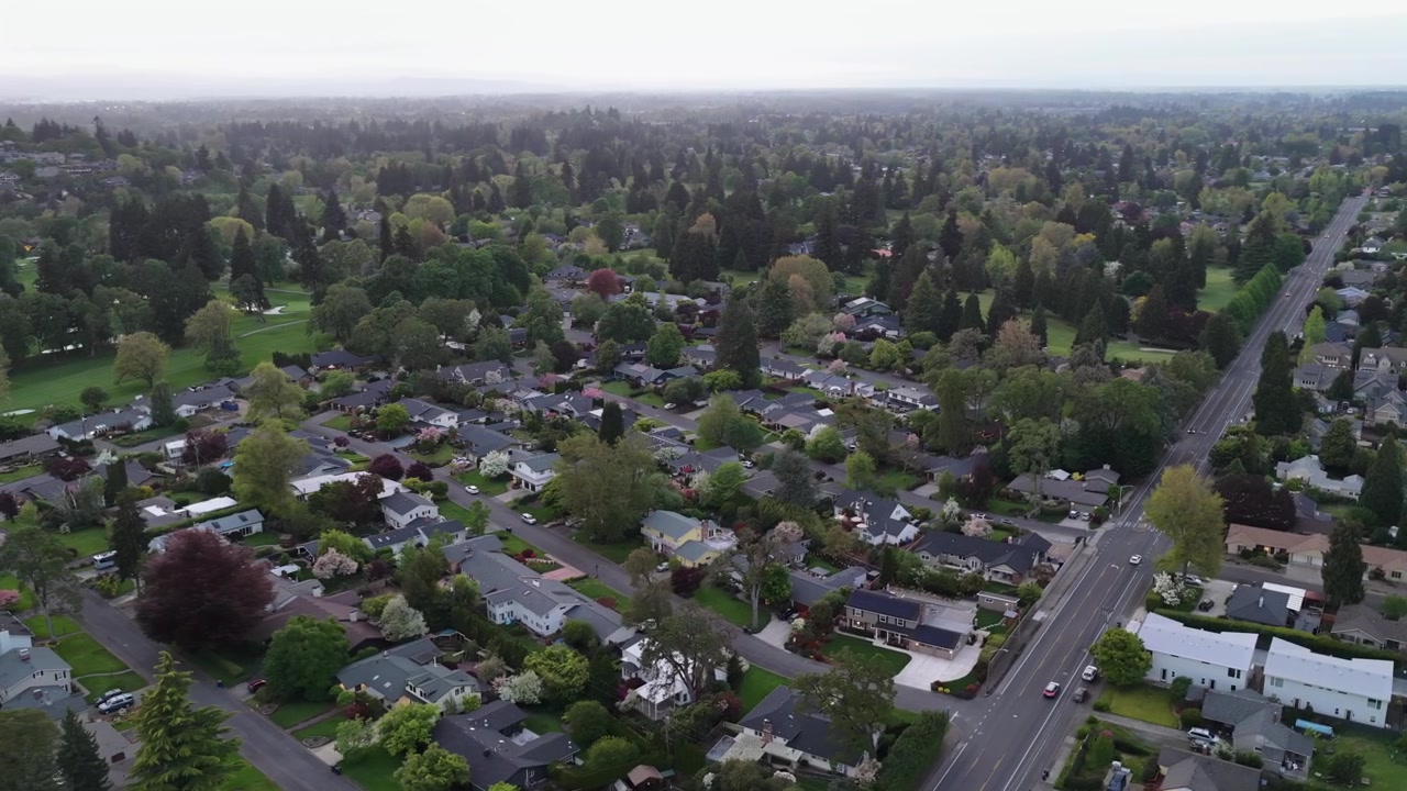 Vasto quartiere residenziale con strade alberate, case unifamiliari, lunga strada principale, campo da golf e fitta chioma arborea sotto un cielo velato e nuvoloso. Eugene, Oregon, USA. Vista aerea. Dall'alto.