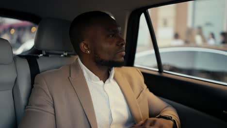 Confident-man-Businessman-with-Black-skin-and-a-beard-in-a-brown-suit-rides-in-a-modern-car-looks-at-his-watch-and-then-out-the-window.-Successful-businessman-driving-in-a-car-to-an-appointed-place