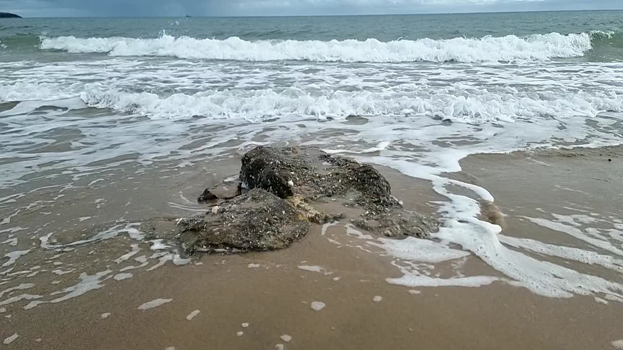 천천히 움직이는 거품 같은 바다의 파도가 글시 해변 해안선에 있는 거친 바위 주변을 고 있다.