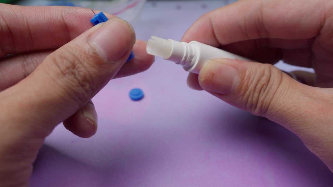 Using a lancet device for blood test preparation with a purple cap and blue lancet on soft purple surface