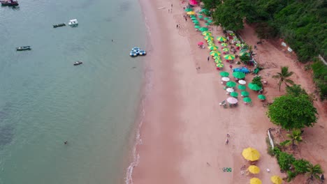 Aerial-view-dolly-in-of-Tartaruga-Beach,-slow-motion-establishing-people-walking-on-the-sand-of-the-beach