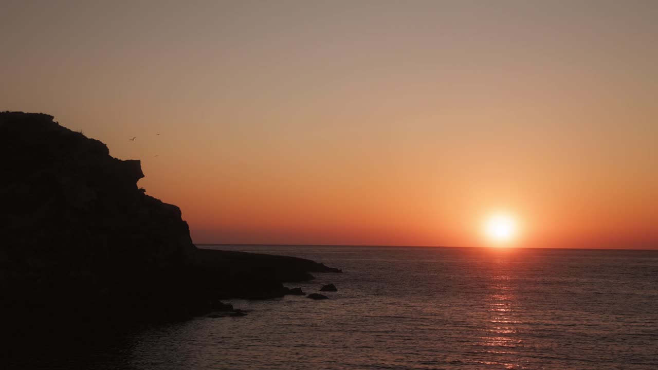 Auringonlaskun kuva Portinatxin lahdella Ibizalla, jossa kultainen heijastus tyynellä Välimerellä ja kallion siluetti