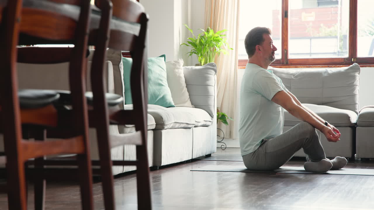 Senior man meditating on yoga mat at home, enjoying peaceful moment