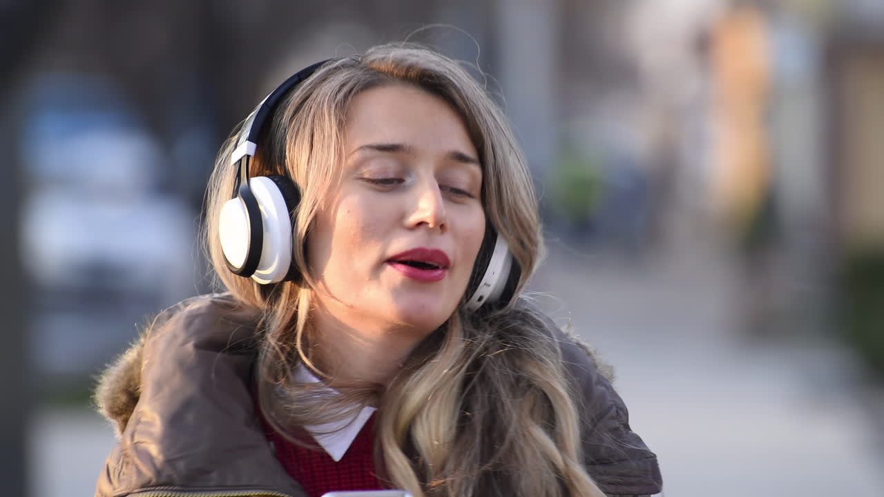 Woman listening to music in her headphones while singing along and dancing in the street