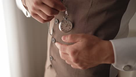 close up of groom securing pocket watch chain into waistcoat before wedding