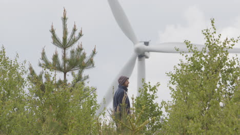 Totale-Aufnahme:-Ein-Gutaussehender-Mann-Bleibt-Bei-Seinem-Spaziergang-Durch-Die-Landschaft-Stehen,-Um-Eine-Windkraftanlage-Zu-Betrachten