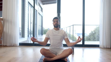 biracial man doing yoga and meditating at home, slow motion