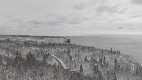 snow-covered trees on shore of lake superior with split rock lighthouse in distance. minnesota, usa. wide aerial shot