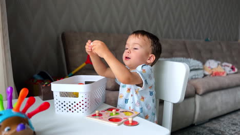 pretty child sits at the desk in his room. lovely baby boy plays with the toys he picks from the white box.