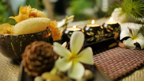 close‑up of decorative candle holders with floral carvings and lit candles, surrounded by spa elements including plumeria flower, natural textures, and warm relaxing ambiance