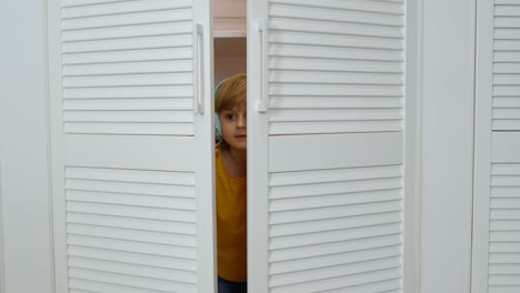 little child girl wearing headphones listening to music and funnily dancing near wardrobe at home