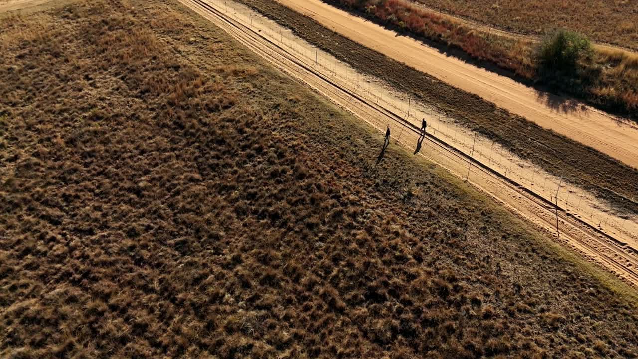 Farm Employees in South Africa patrol perimeter fence on foot, checking for signs of animals escaping during the dry winter season