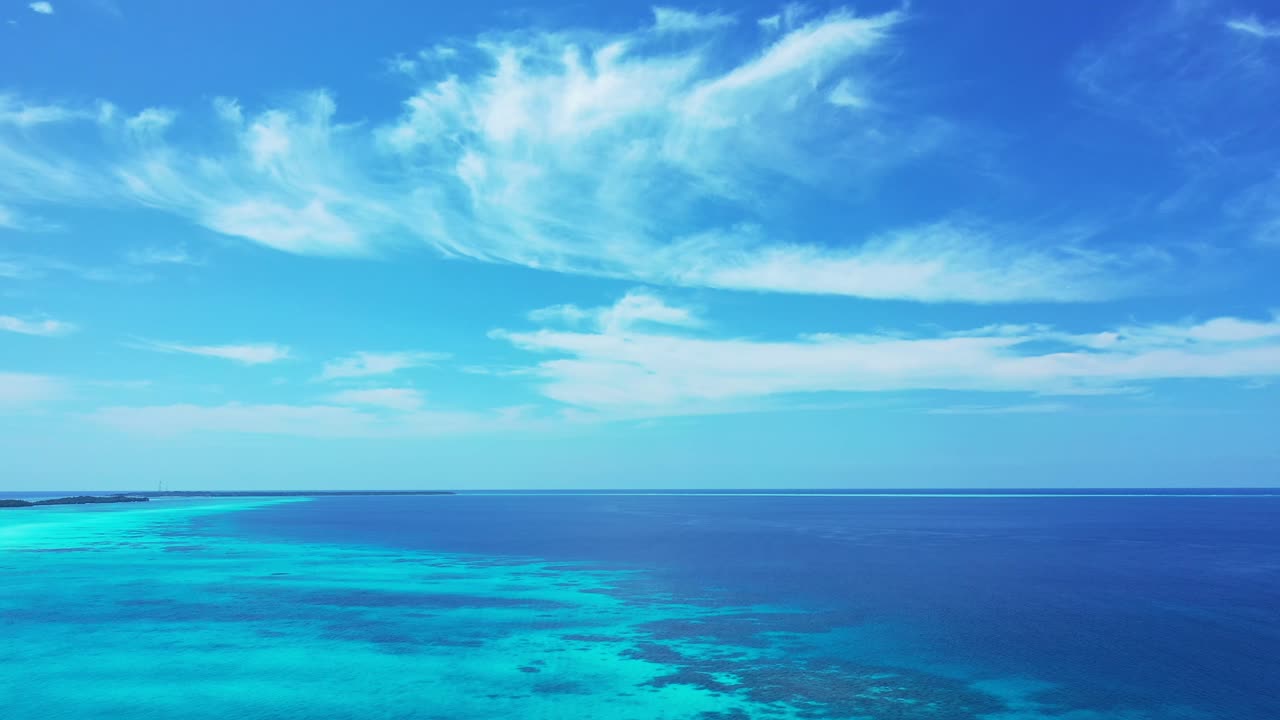 Peaceful scenery of bright sky with white veil of clouds over blue turquoise Indian sea around low-lying tropical islands