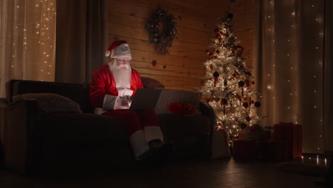 santa claus working on laptop sends letters with wishes or congratulations by email for christmas or new year. santa communicates on social networks with children around world.