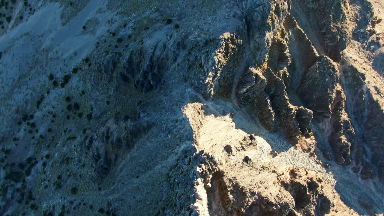 Captivating aerial footage of Nevado de Colima's rugged mountains in golden light. High-altitude view reveals intricate rocky textures, vivid shadows, and breathtaking natural beauty