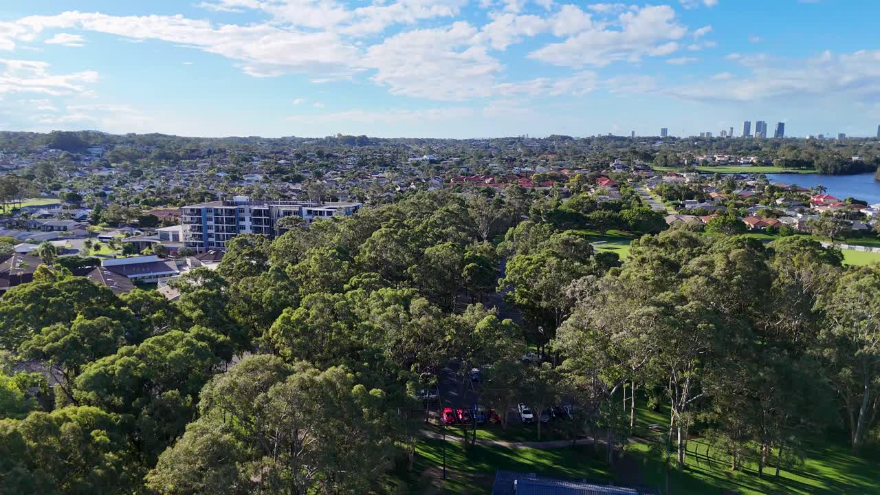 Drone footage captures lush parkland and urban skyline under bright daylight in Gold Coast, Australia. Vibrant greenery and city views