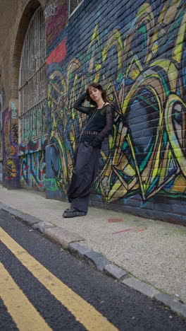 Vertical-Video-Outdoor-Fashion-Portrait-Of-Young-Alternative-Style-Woman-Leaning-Against-Graffitti-Covered-Wall-In-London-City-Street-UK-In-Real-Time