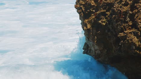 ocean waves with foam splashing against coral boulder, detail shot