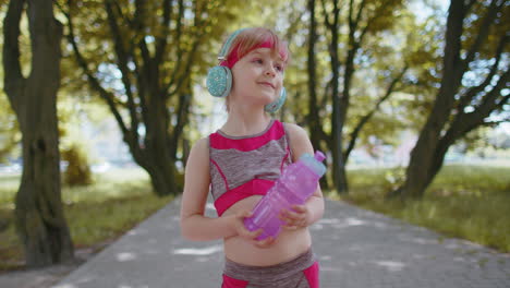 corredora deportiva niña niña con auriculares escuchando su canción favorita sosteniendo una botella de agua