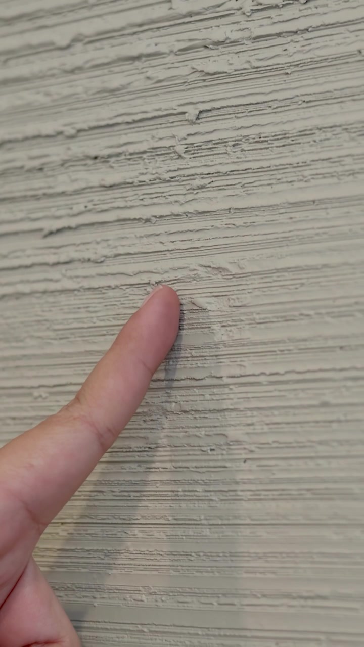 Static close-up shot of a hand pointing at a rough, grey concrete textured wall surface.
