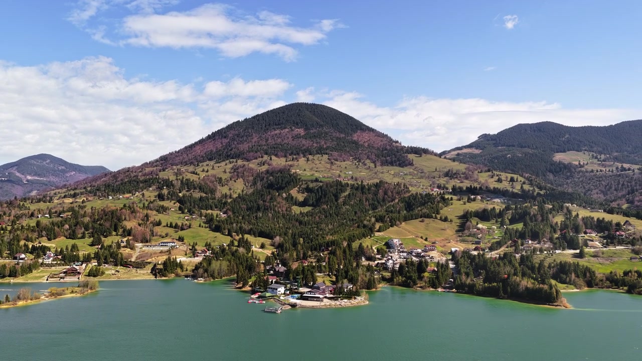 Veduta aerea con drone che mostra il lago Colibita e le colline circostanti con case sparse e foresta, in Romania