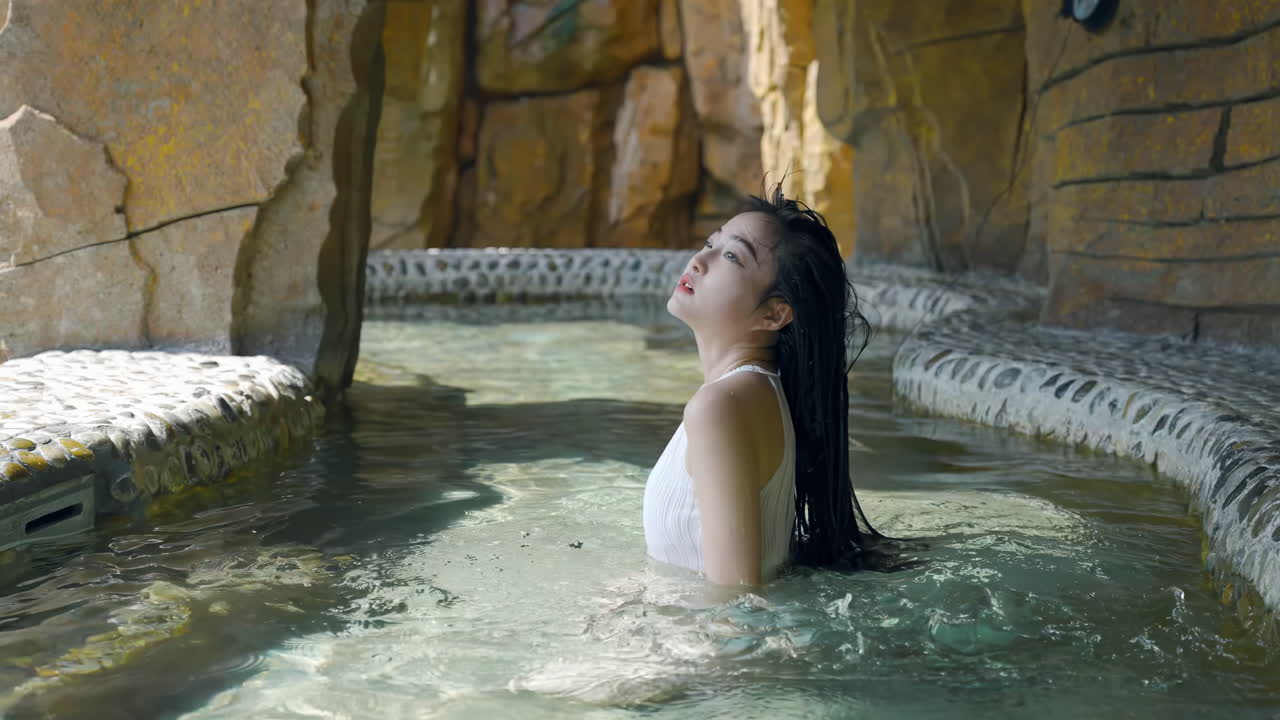 Bella giovane donna che si rilassa in una spa termale naturale, con i lunghi capelli sciolti, si gode un onsen tradizionale in una piscina termale calda all'aperto all'alba, per il turismo del benessere e delle spa.