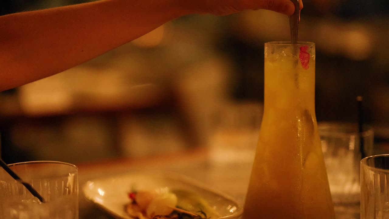A hand stirs a cocktail in a dimly lit setting, creating a warm, inviting atmosphere. Captured on the Gold Coast, Australia
