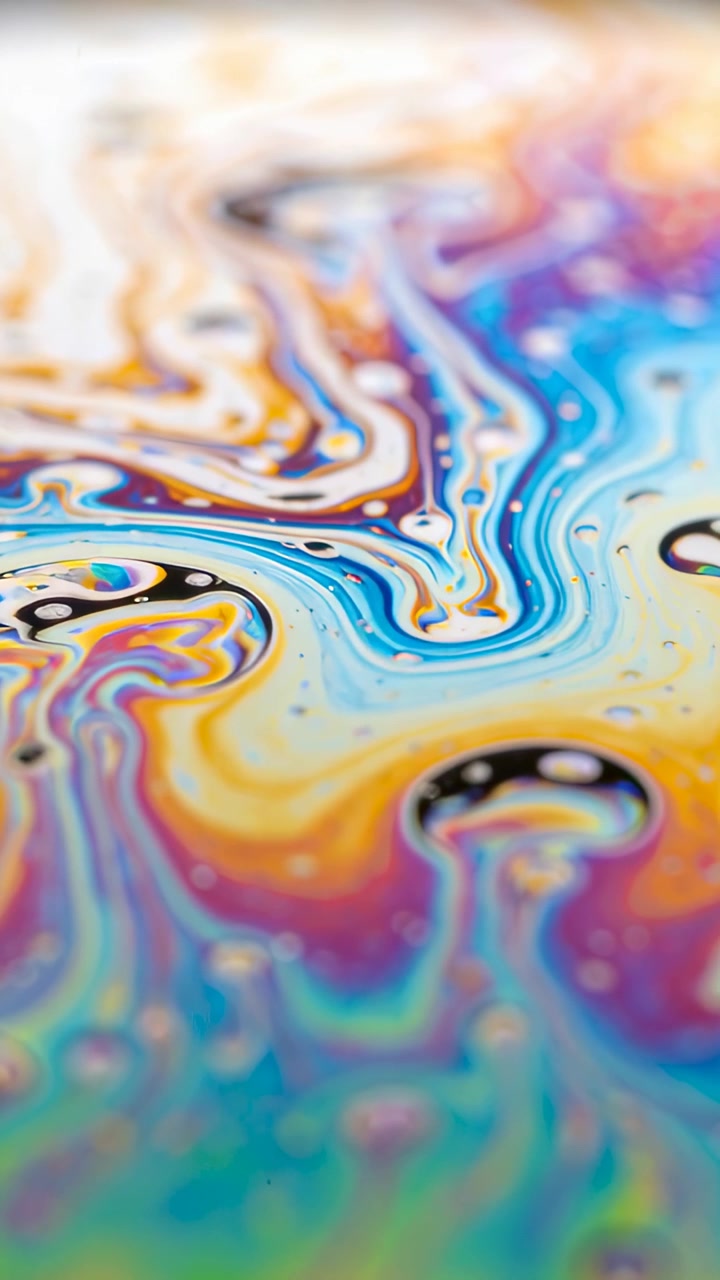 Video verticale: Che mostra una pellicola sottile che si sposta su un tavolo, con la tensione che crea bande di colore e macchie scure.