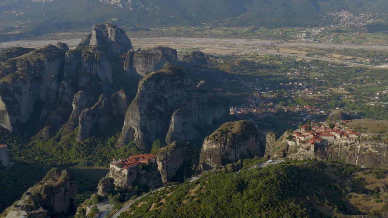 Cinematic aerial view of Meteora monastery in Greece perched on towering cliffs, dramatic rock formations and lush green valley create a breathtaking historic scene