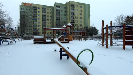 la nieve está cayendo en un pequeño patio de recreo en los suburbios de una ciudad