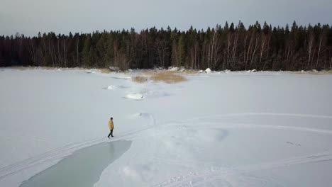 Drohnenschuss,-Gefolgt-Von-Einem-älteren-Mann,-Der-Auf-Einem-Zugefrorenen-Wintersee-In-Nordfinnland-Spazieren-Geht,-Weit-Weg-Von-Der-Zivilisation