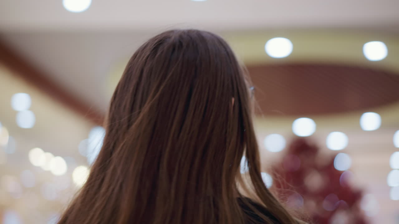 현대 쇼핑몰에서 상하는 안경을 입은 여성의 클로즈업 후방 헤드 뷰, 부드러운 보케 조명이 배경을 조명합니다.