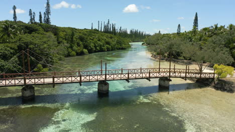 Eine-Hölzerne-Fußgängerbrücke-über-Einen-Flachen-Wasserkanal-Zwischen-Der-Isle-Of-Pines-Und-Der-Insel-Kotomo,-Neukaledonien,-Antenne