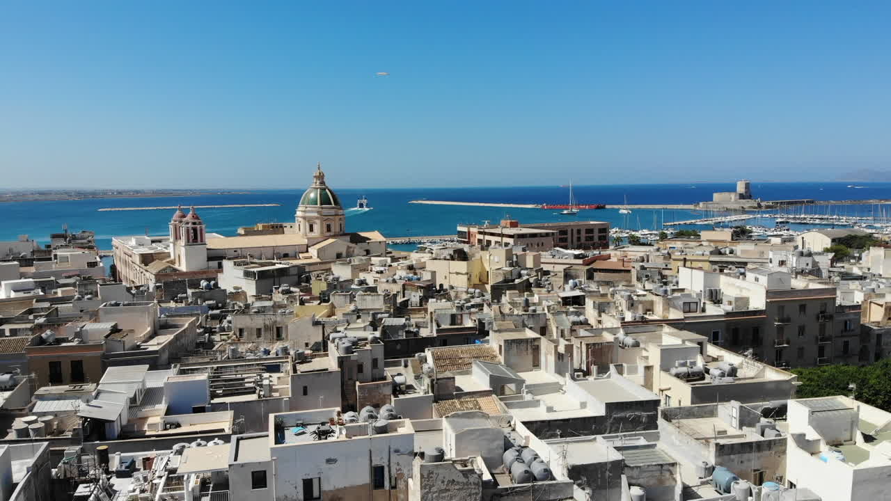 A smooth forward drone flight over Trapani’s old town, showcasing the dense rooftops, the green dome of Chiesa del Purgatorio, and the bright blue Mediterranean Sea in the background