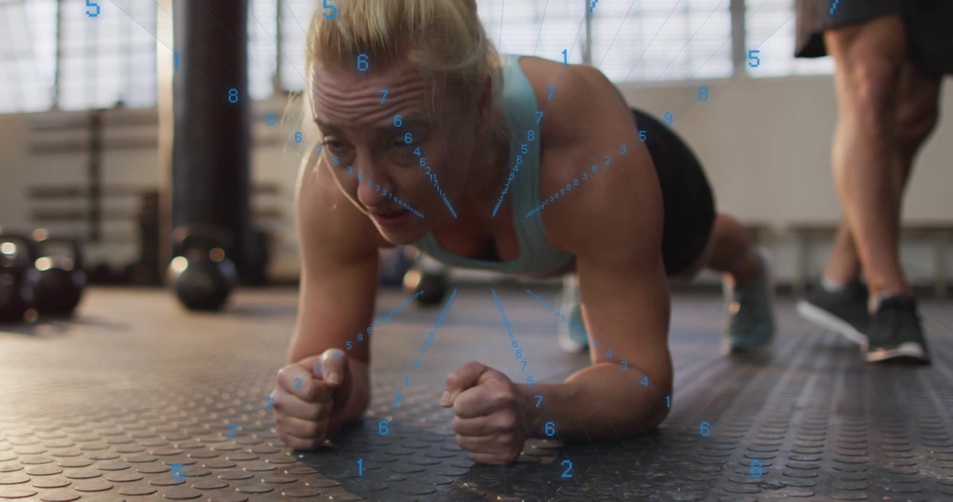 Female trainee holding forearm plank in gym, trainer cueing while blue HUD overlay tracking form