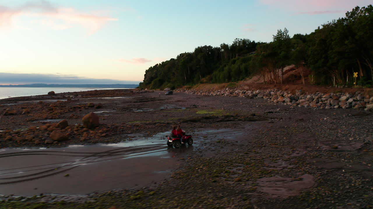 海岸の岩だらけのビーチで四輪バイクに乗る人々を追いかける空撮写真、夕方の日差し