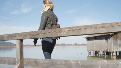 slow motion shot of a woman walking down a jetty to a small hut on a reflective clear mountain lake