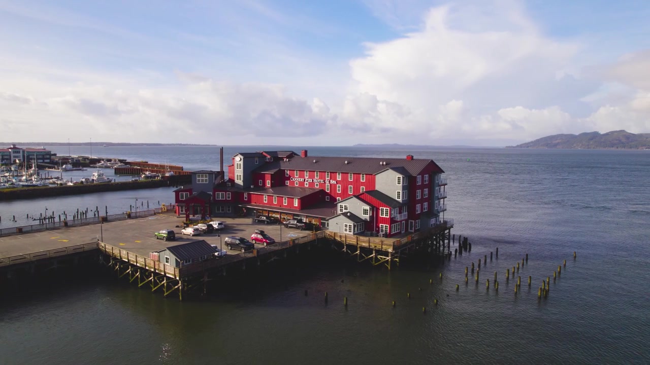 Una ripresa aerea rivela un lungo edificio rosso appollaiato su un molo, che si estende sul vasto fiume Columbia con panorami sereni