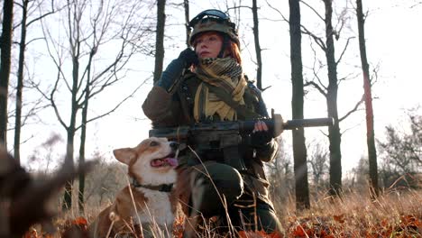 young pretty redhead woman in military uniform armed with rifle playing with dog