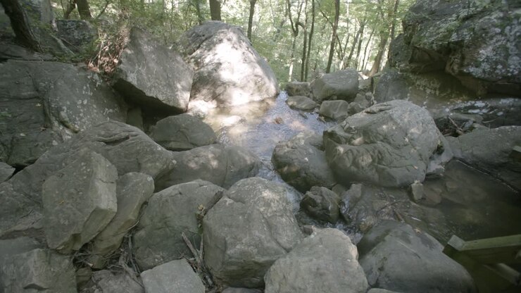Slow motion wide shot of a small stream meandering through a group of rocks and boulders