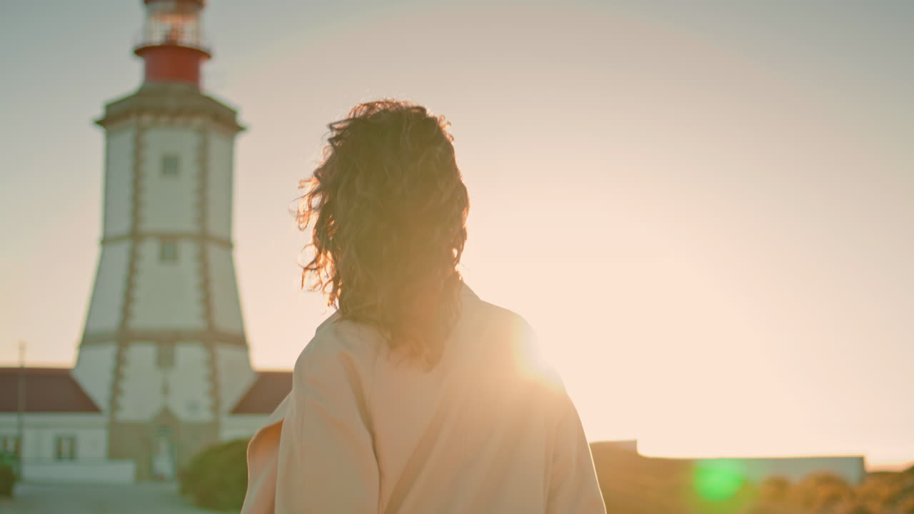 Attraktiv pige leger med solen ved fyrtårnet. Ubekymret kvinde går tur ved havet om aftenen.