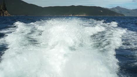 parte trasera de las olas del barco con cielo azul y montañas en segundo plano.
